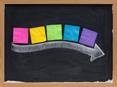 timeline concept - blank colorful sticky notes along thick white chalk arrow on blackboard with copy space